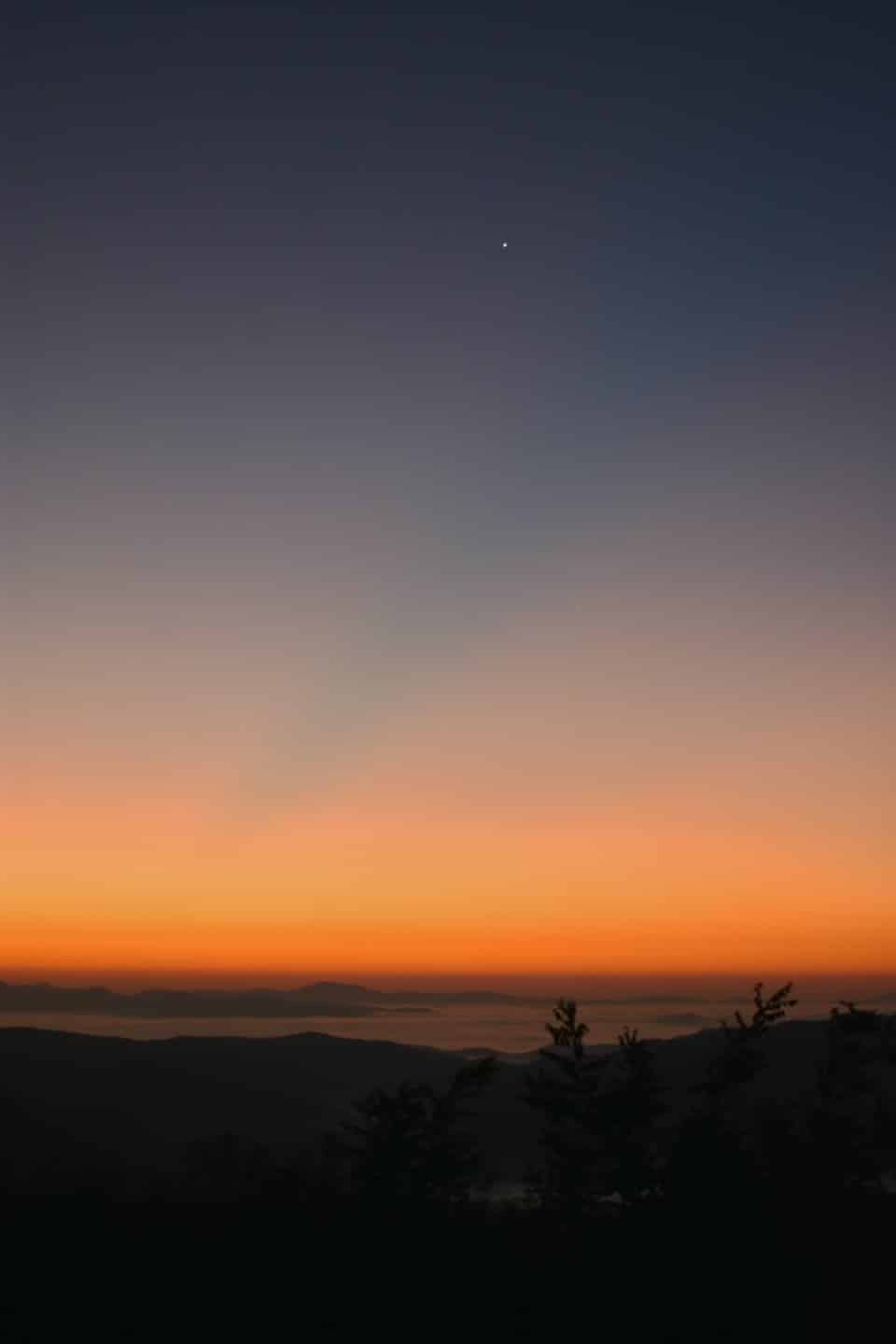 La nebbia si posa nelle valli sotto montagne silhouette al crepuscolo.