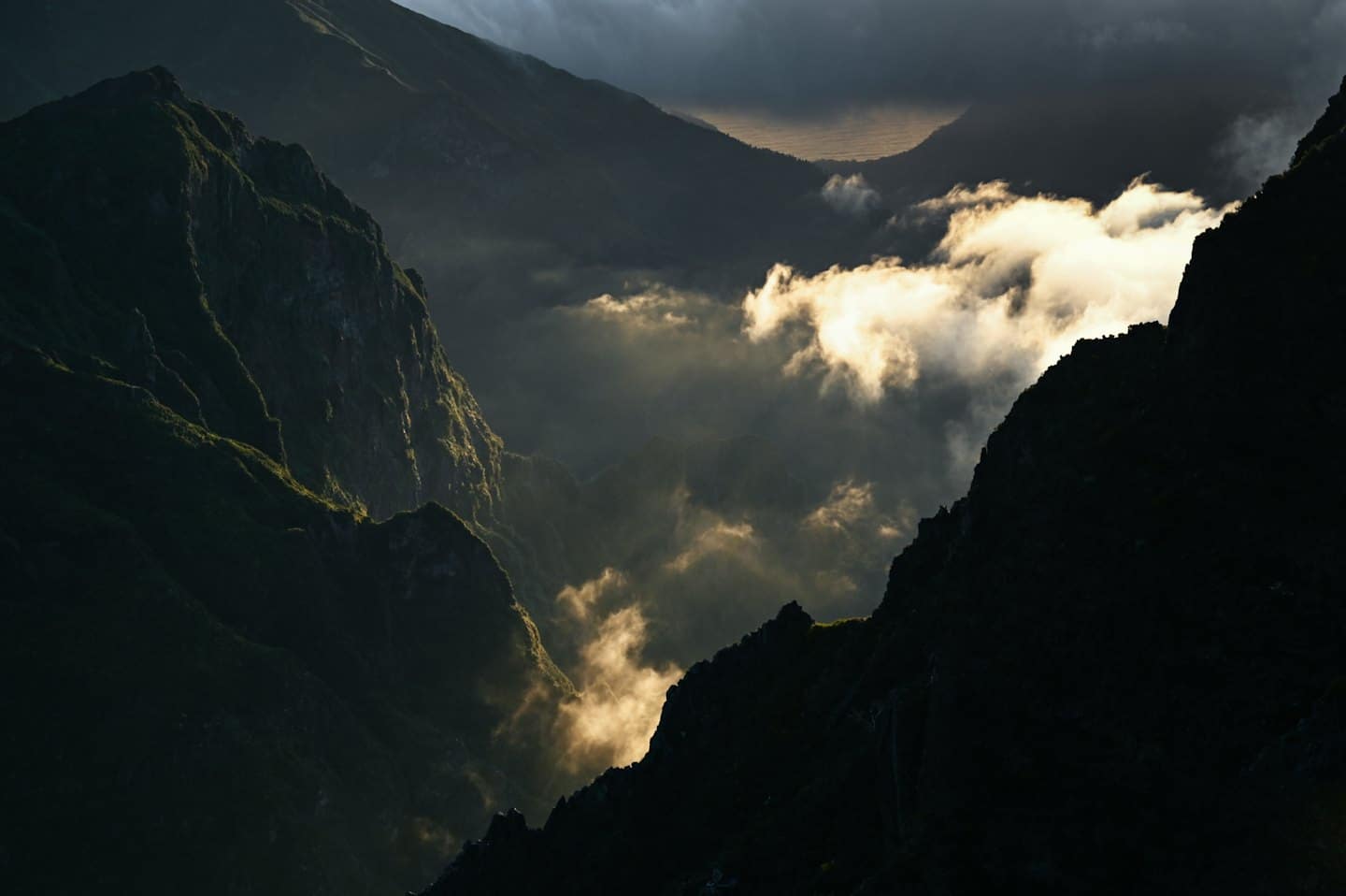La luce del sole splende sulle cime montuose frastagliate parzialmente coperte dalla nebbia.