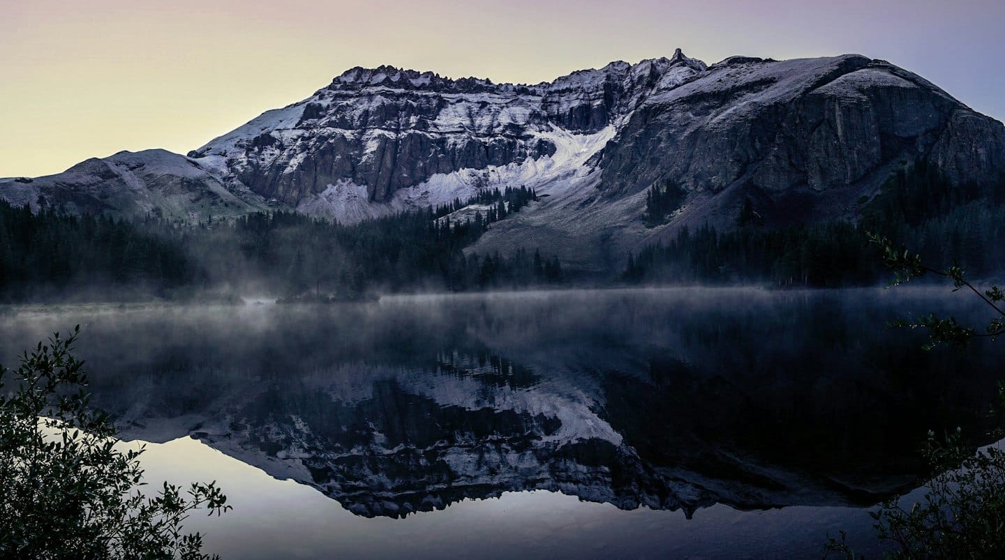 Montagne innevate riflesse in un lago calmo all'alba.