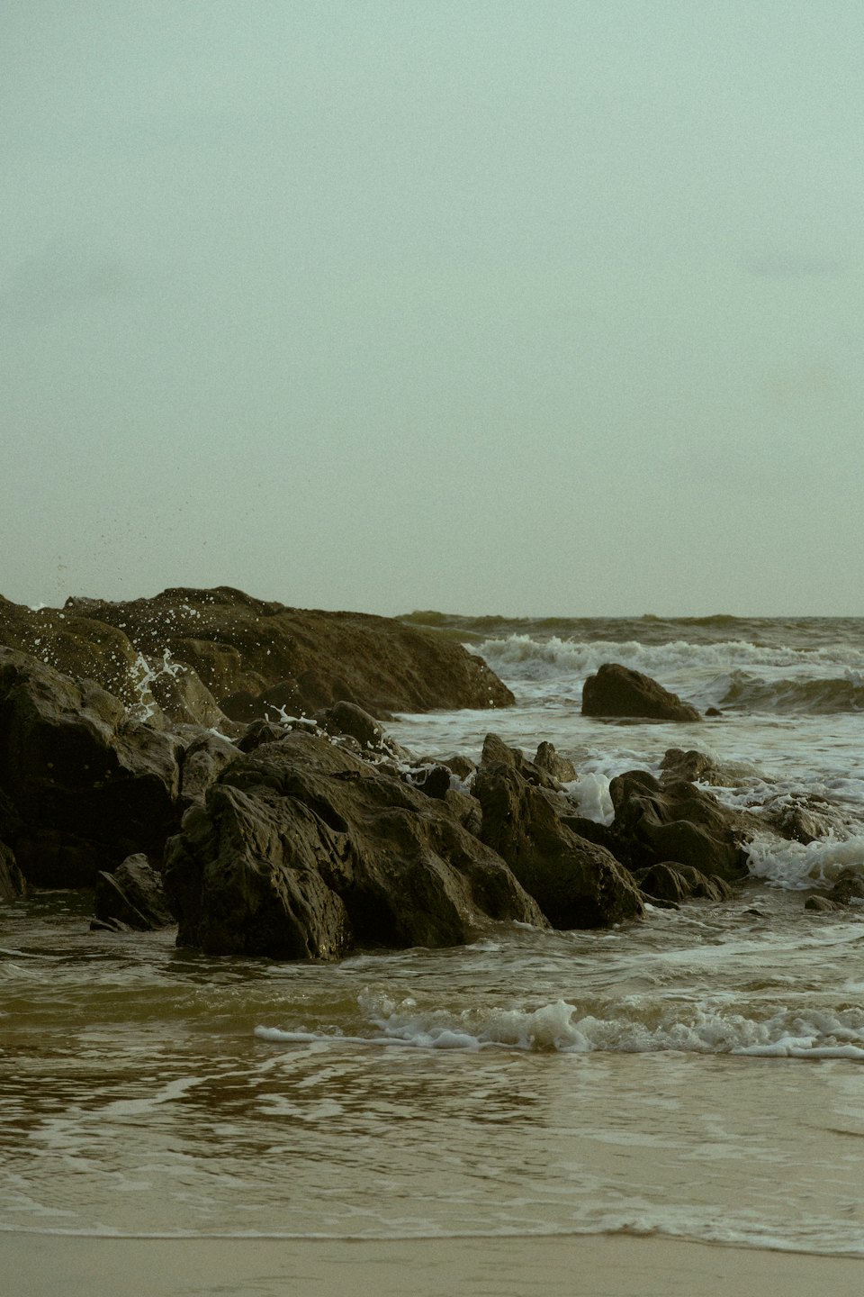 Onde dell'oceano si infrangono su scogli scuri e frastagliati lungo la costa.