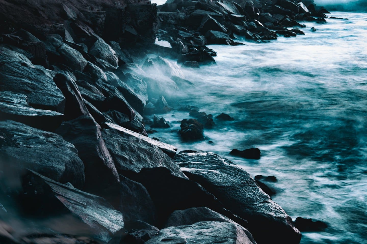 Onde nebbiose dell'oceano che si infrangono su una costa rocciosa e scura.