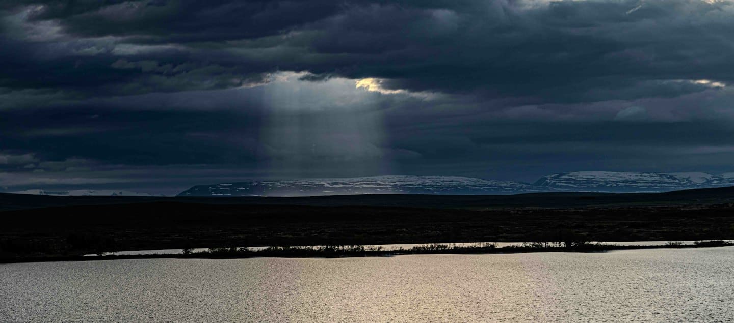Lago sereno che riflette la luce del sole vicino a terra brulla e montagne.
