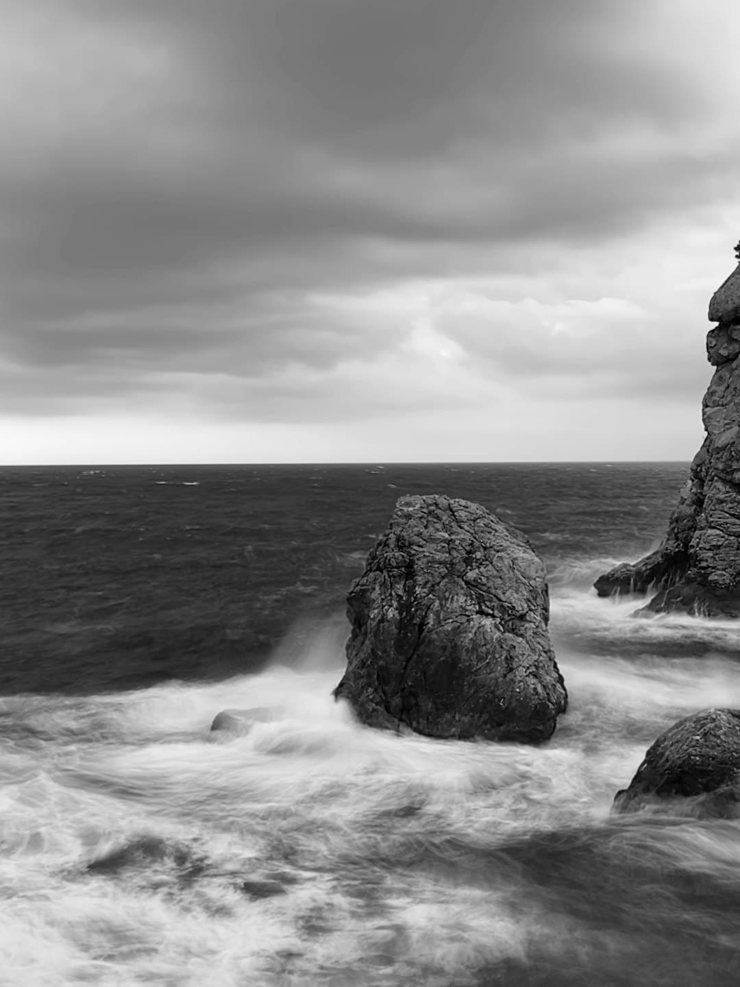 Onde dell'oceano si infrangono su rocce scure sotto un cielo nuvoloso.